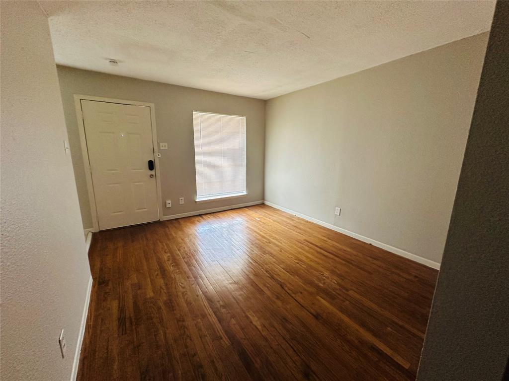 Room featuring wood-finish flooring, neutral wall paint, a six-panel entry door, and a window with integrated blinds