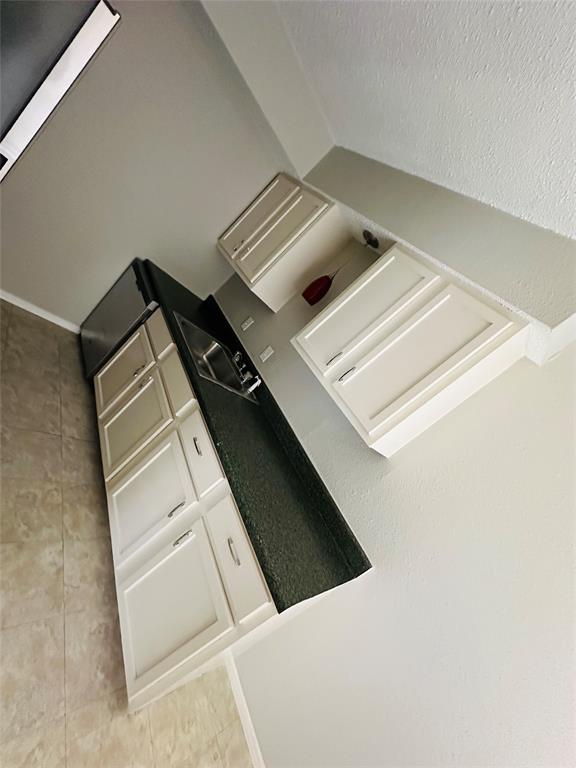 Kitchenette featuring shaker-style cabinetry, dark stone-finish countertops, stainless steel sink, and ceramic tile flooring