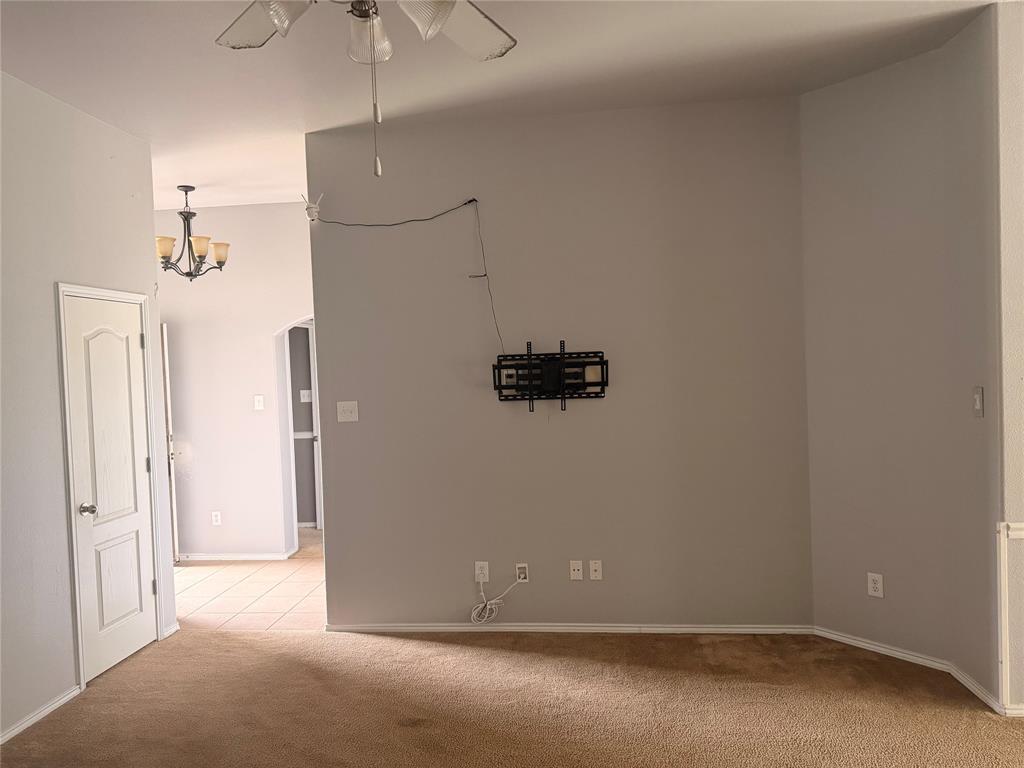 Neutral interior space featuring high ceilings, a wall-mounted media bracket, a central ceiling fan with integrated lighting, and a multi-light chandelier Neutral interior space featuring high ceilings, a wall-mounted media bracket, a central ceiling fan with integrated lighting, and a multi-light chandelier