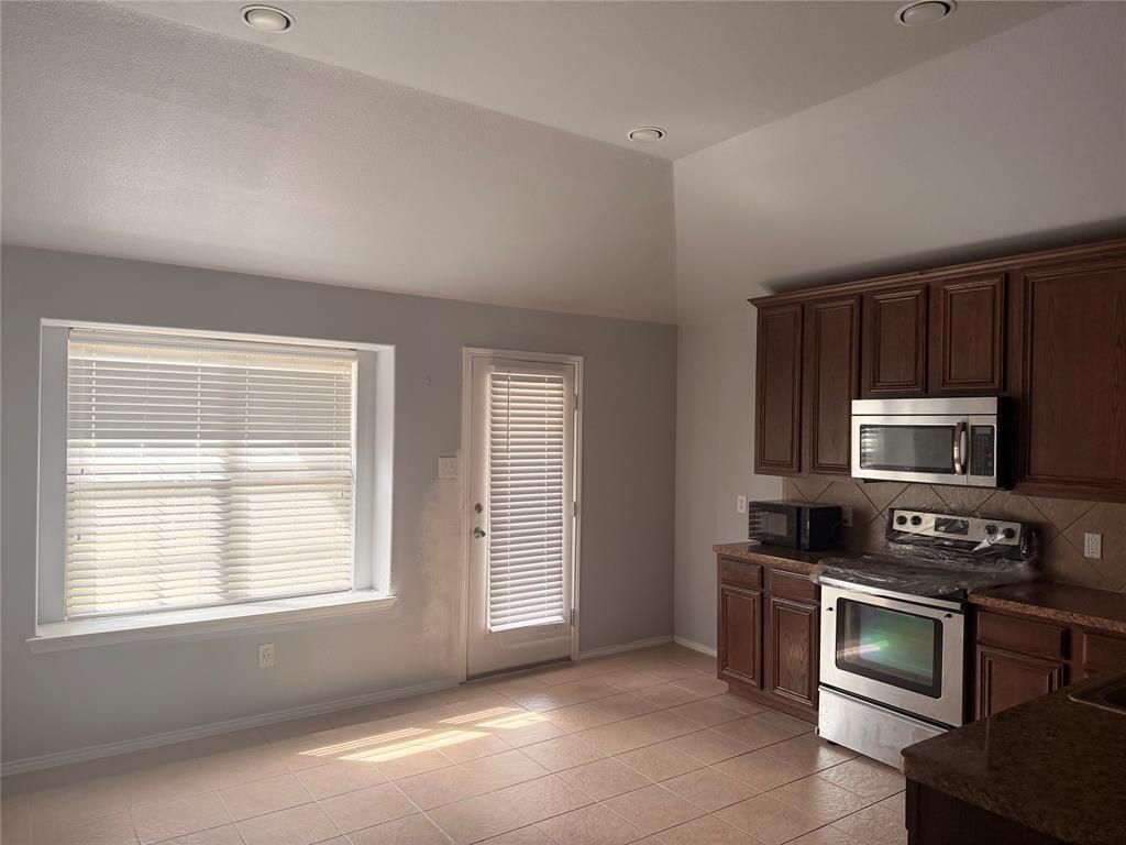 Kitchen featuring vaulted ceilings, recessed lighting, tile flooring, dark-finish cabinetry, and stainless-steel appliances Kitchen featuring vaulted ceilings, recessed lighting, tile flooring, dark-finish cabinetry, and stainless-steel appliances