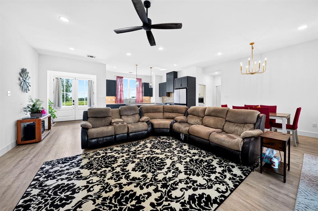 Open-concept main room featuring wood-finish flooring, recessed lighting, a matte black ceiling fan, and a multi-light chandelier Open-concept main room featuring wood-finish flooring, recessed lighting, a matte black ceiling fan, and a multi-light chandelier