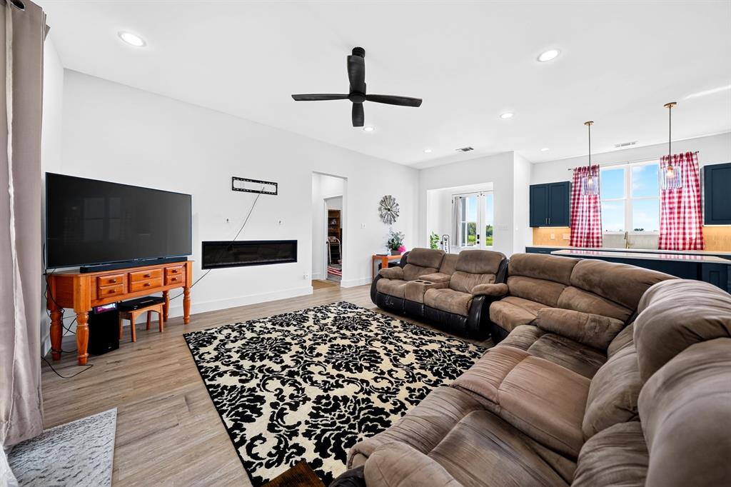 Open-concept living space featuring wood-finish flooring, recessed lighting, a linear wall-mounted electric fireplace, and a ceiling fan with matte black finish Open-concept living space featuring wood-finish flooring, recessed lighting, a linear wall-mounted electric fireplace, and a ceiling fan with matte black finish