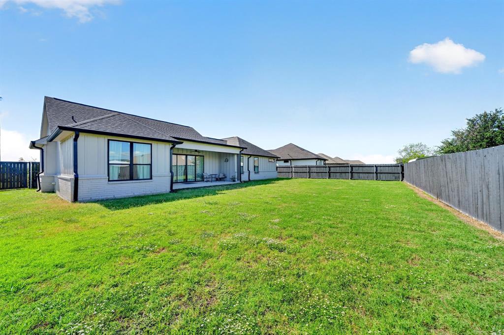 Expansive backyard featuring a manicured lawn, full privacy fencing, and a covered patio area with neutral-toned brick and siding exterior