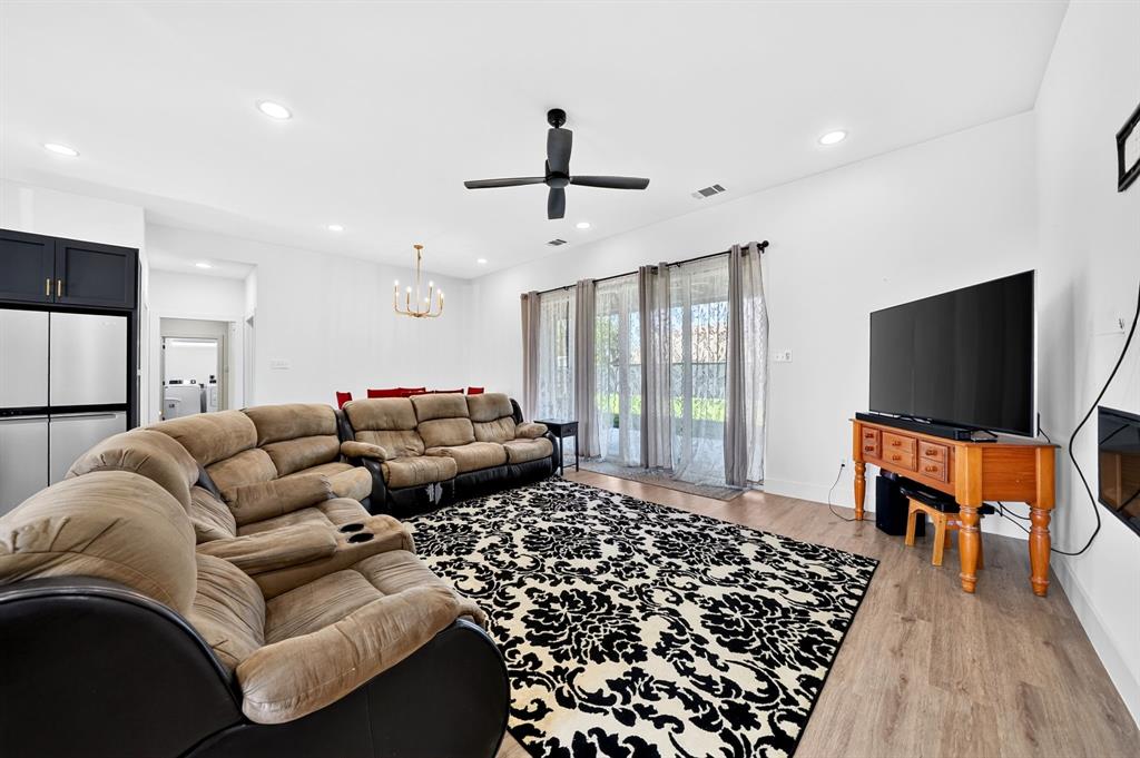 Open-concept living space featuring wood-finish flooring, recessed lighting, a matte black ceiling fan, and large sliding glass doors Open-concept living space featuring wood-finish flooring, recessed lighting, a matte black ceiling fan, and large sliding glass doors