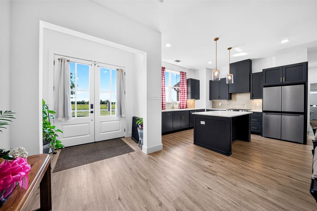 Kitchen featuring dark cabinetry, a central island with a stone countertop, stainless steel refrigerator, recessed lighting, and wood-finish flooring Kitchen featuring dark cabinetry, a central island with a stone countertop, stainless steel refrigerator, recessed lighting, and wood-finish flooring