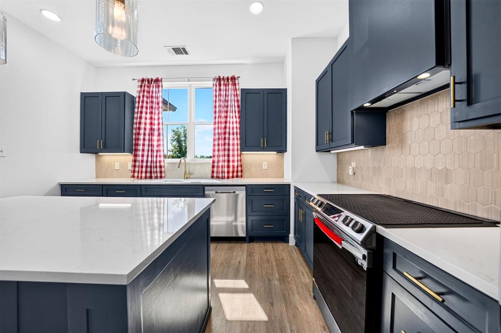 Kitchen featuring navy blue shaker-style cabinetry, a central island with a quartz countertop, hexagonal tile backsplash, wood-finish flooring, and stainless steel appliances