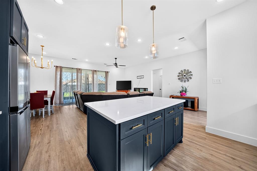 Kitchen featuring a center island with dark cabinetry, white stone-finish countertop, dual pendant lighting, and wood-finish flooring