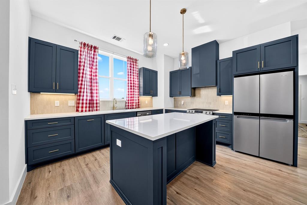 Kitchen featuring navy blue cabinetry, center island with white quartz countertop, stainless steel refrigerator, textured tile backsplash, and wood-finish flooring