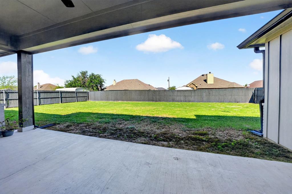 Covered patio featuring a concrete floor, high-ceiling structure, and integrated overhead fan, overlooking a fenced backyard with a lawn