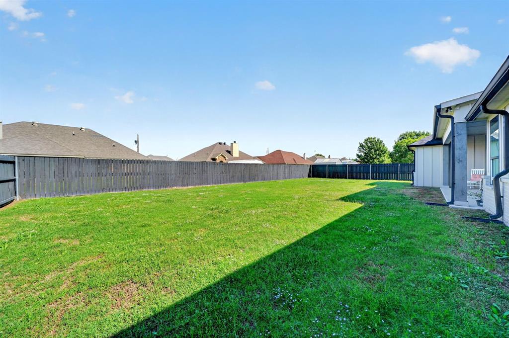 Expansive backyard featuring a level lawn, full-perimeter wood fencing, and a covered patio area
