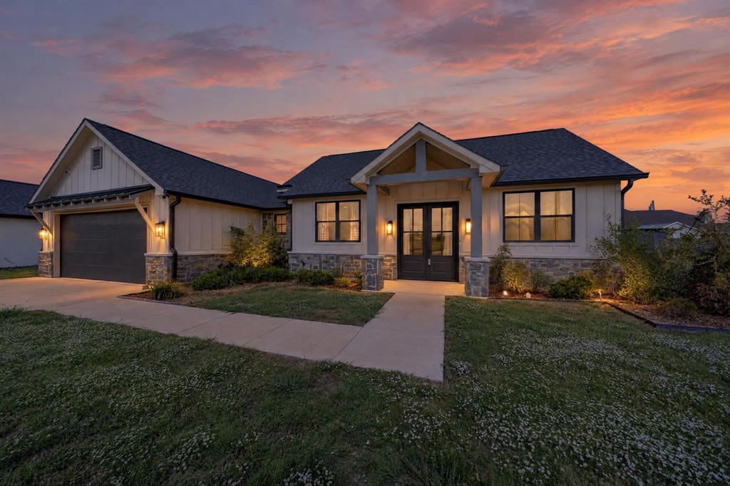Modern exterior featuring vertical board-and-batten siding, stone veneer accents, gabled roofline, covered front entryway with timber-style columns, and an attached multi-car garage Modern exterior featuring vertical board-and-batten siding, stone veneer accents, gabled roofline, covered front entryway with timber-style columns, and an attached multi-car garage