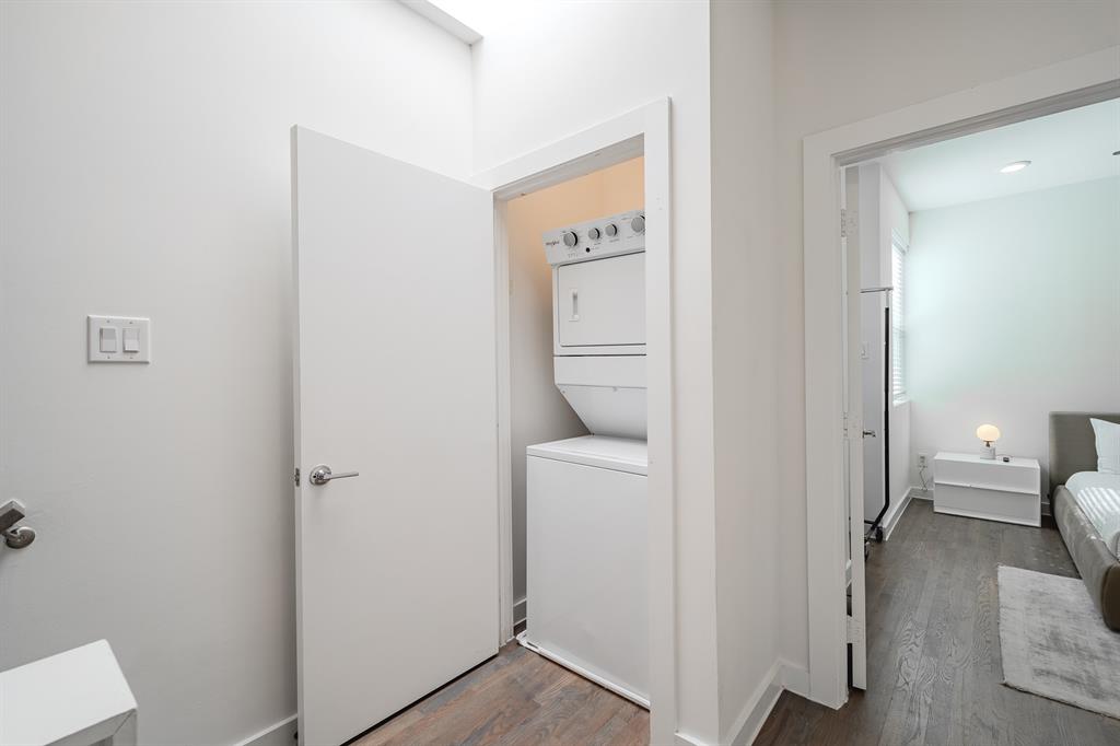 Laundry closet containing a stacked washer and dryer unit, featuring wood-finish flooring and a skylight