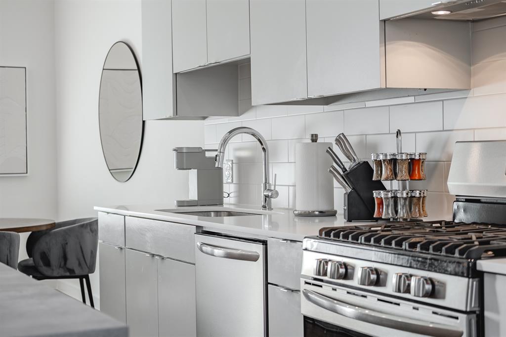Kitchen featuring flat-panel cabinetry, light-toned stone-finish countertops, subway tile backsplash, and stainless steel appliances including a gas range and undermount sink with a gooseneck faucet