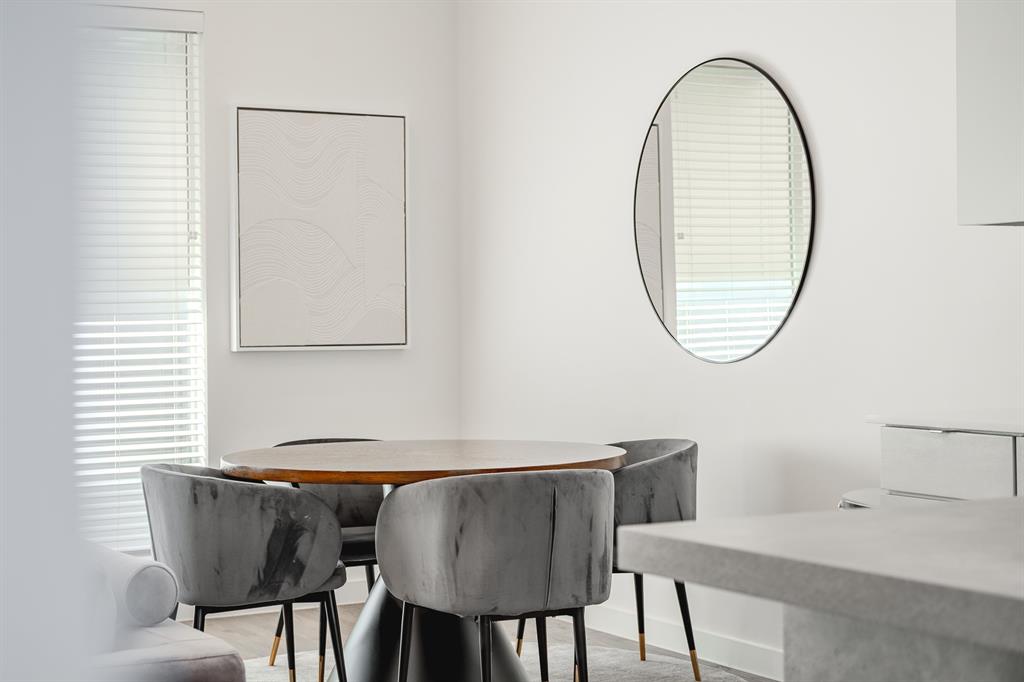Neutral-toned interior space featuring horizontal slat blinds, a circular wall-mounted mirror with a black frame, and wood-finish flooring