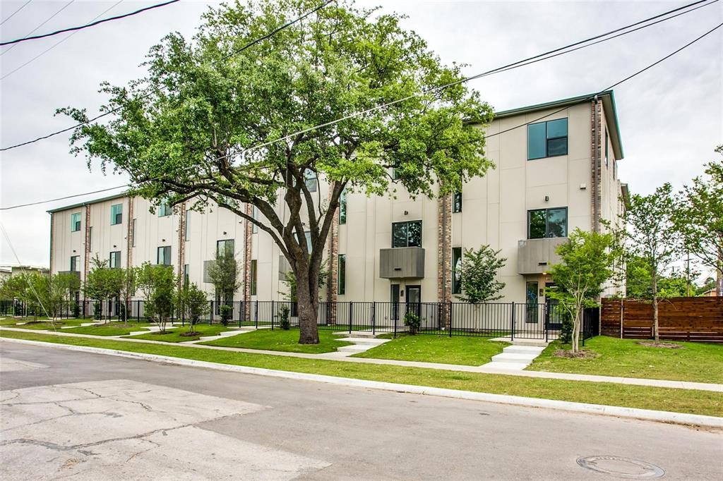 Multi-story exterior featuring a neutral smooth panel facade, brick masonry accents, metal balcony railings, and a fenced front perimeter