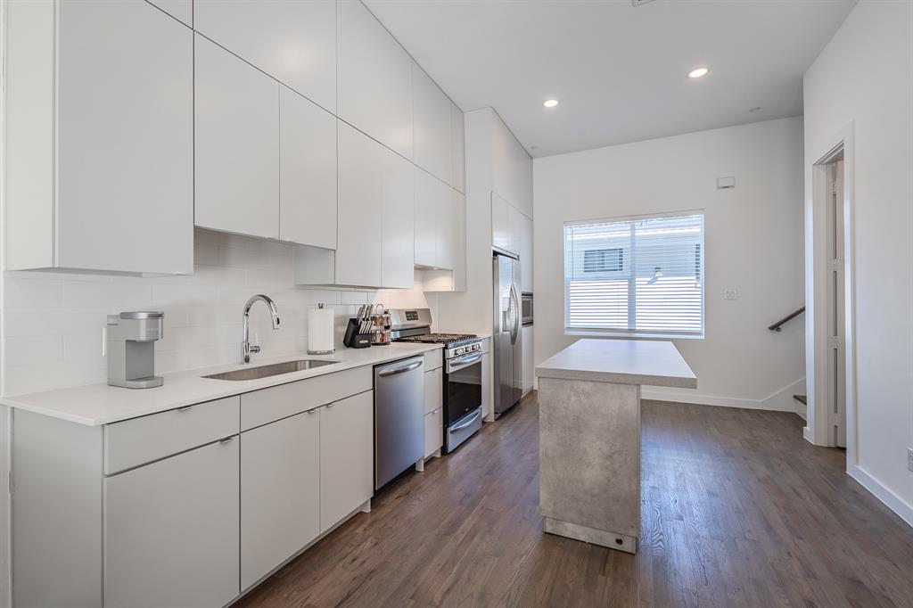 Kitchen featuring floor-to-ceiling cabinetry, stainless steel appliances, stone-finish island, wood-finish flooring, and recessed lighting