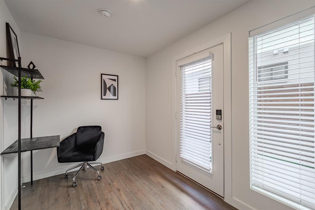 Interior space featuring wood-finish flooring, white walls, large window with horizontal blinds, and a glass-paneled exterior door with integrated blinds and electronic deadbolt hardware