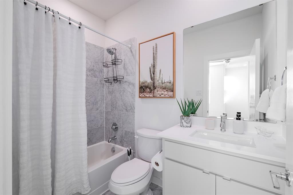 Bathroom featuring a white vanity with a composite countertop and integrated sink, a large wall-mounted mirror, and a tub-shower combination with floor-to-ceiling stone-finish tile surround