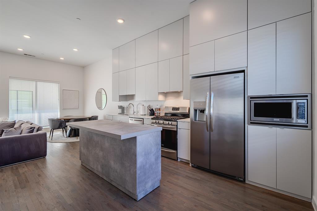 Kitchen featuring full-height flat-panel cabinetry, stone-finish kitchen island, stainless steel appliances, and wood-finish flooring