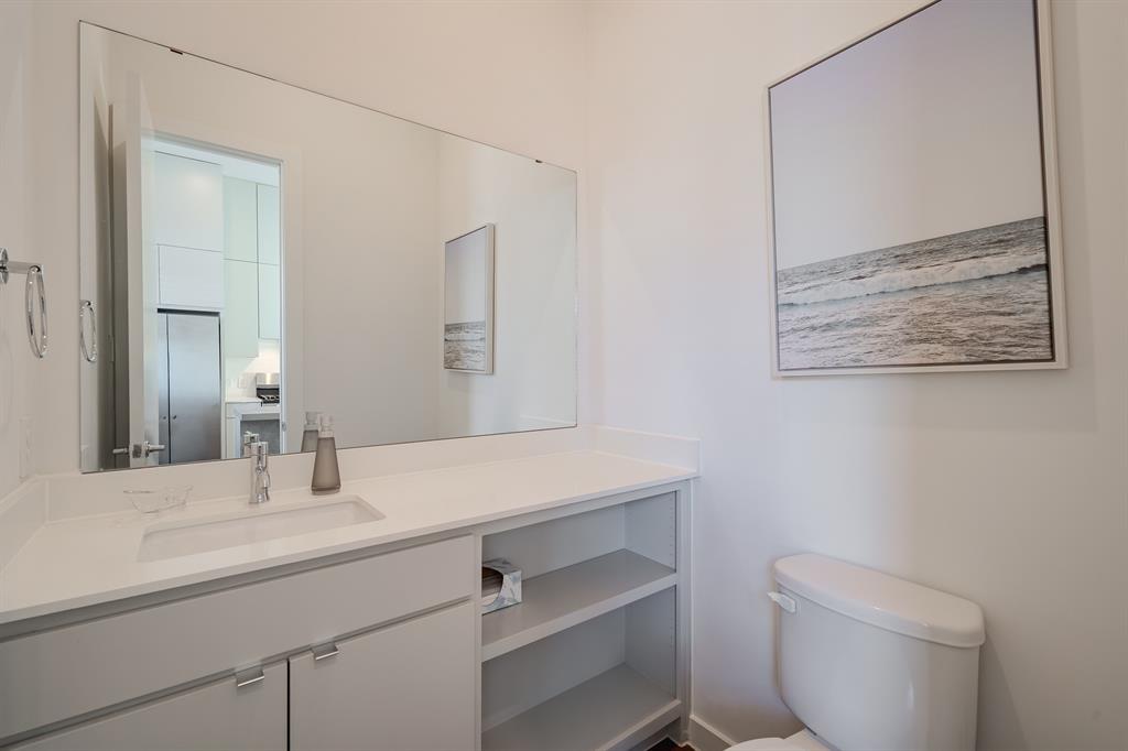 Custom vanity featuring a light gray finish, solid-surface countertop with an integrated rectangular sink, polished chrome faucet, and open lower shelving, complemented by a wall-to-wall mirror and chrome towel ring