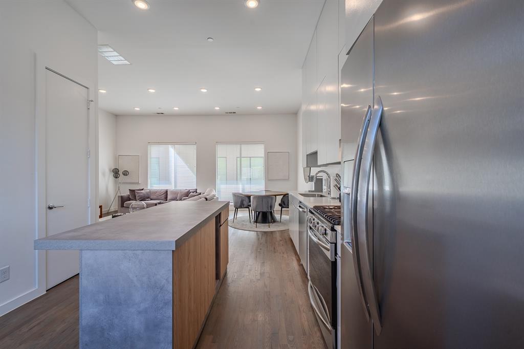 Kitchen island with concrete-style countertop and wood-finish cabinetry, stainless steel appliances, recessed ceiling lighting, and wood-finish flooring