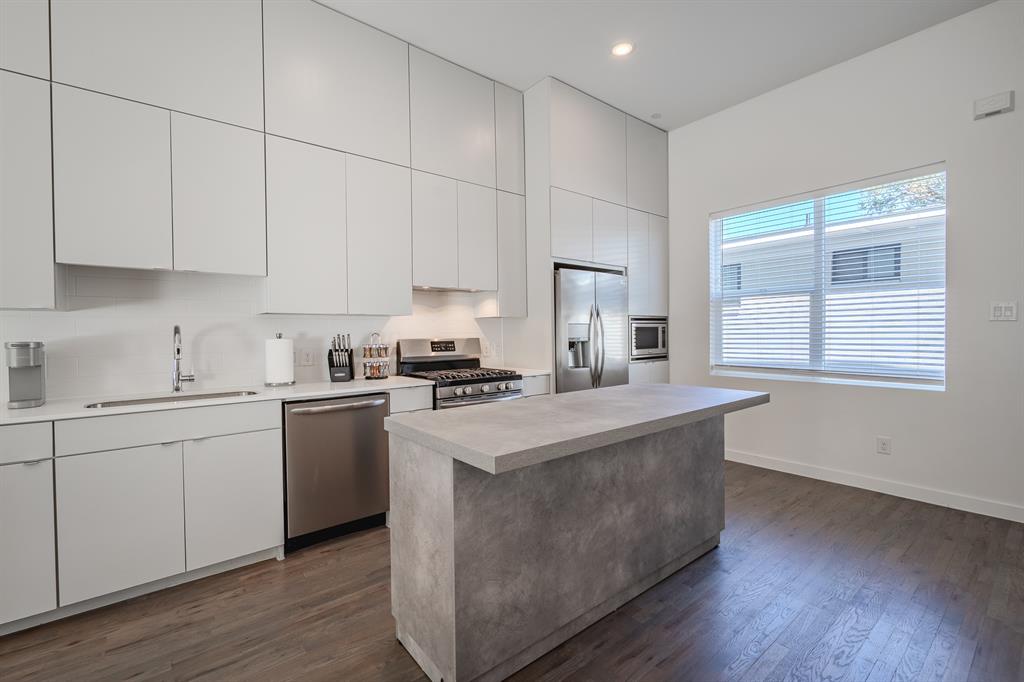 Kitchen featuring floor-to-ceiling white cabinetry, wood-finish flooring, a central island with a stone-finish countertop, and stainless steel appliances