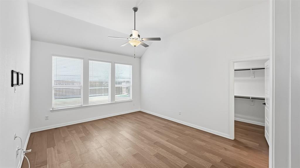 Vaulted ceilings, wood-finish flooring, ceiling fan with integrated light fixture, three-panel window configuration, and walk-in closet with built-in shelving