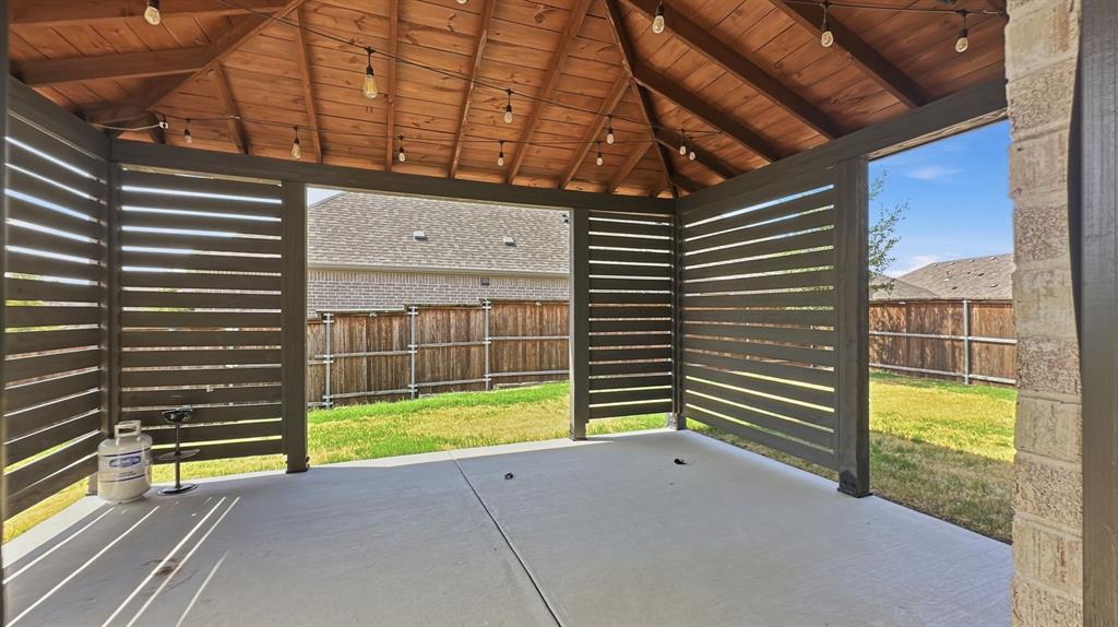 Covered patio featuring a wood-plank ceiling, horizontal slat privacy screening, concrete flooring, and built-in string lighting