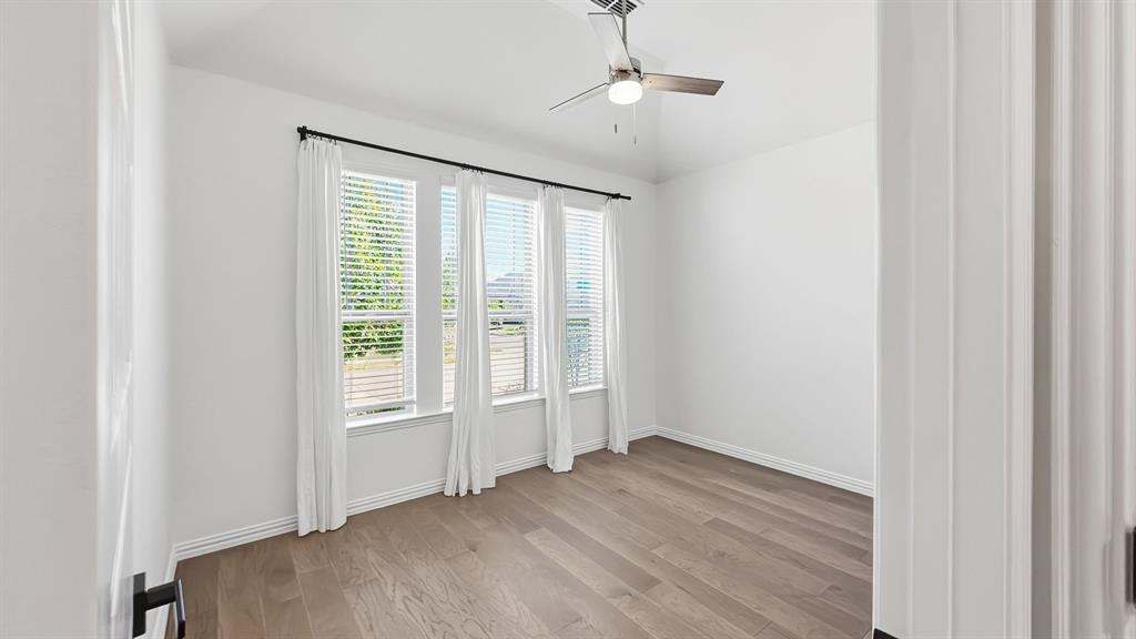 Room featuring wood-finish flooring, high ceilings, a modern brushed-nickel ceiling fan, and three large windows with neutral wall finishes