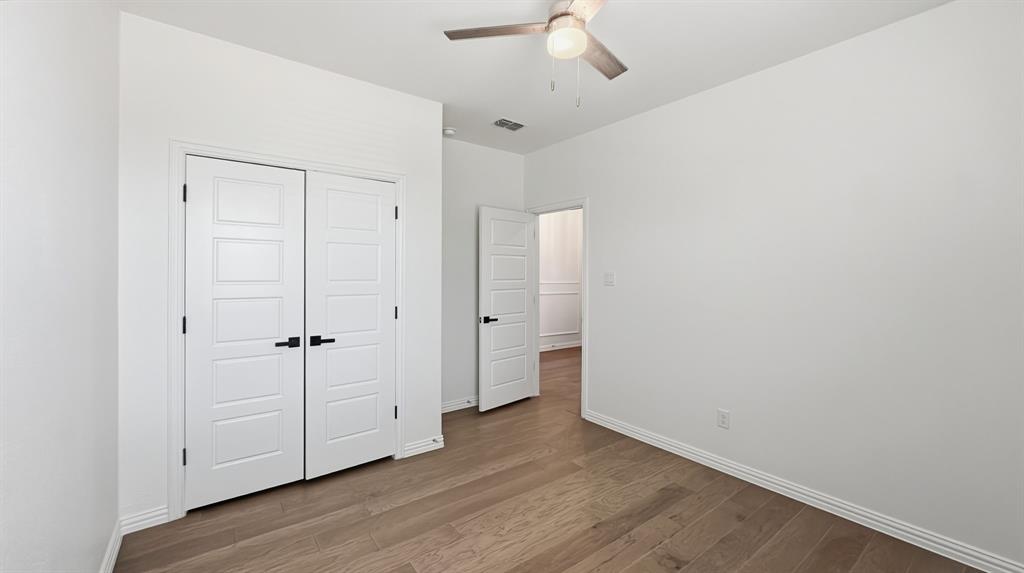 Wood-finish flooring, double-panel closet doors with matte black hardware, and a ceiling fan with integrated lighting