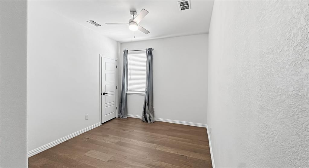 Interior room featuring wood-finish flooring, a neutral color palette, a ceiling fan with integrated lighting, and a multi-panel door with matte black hardware