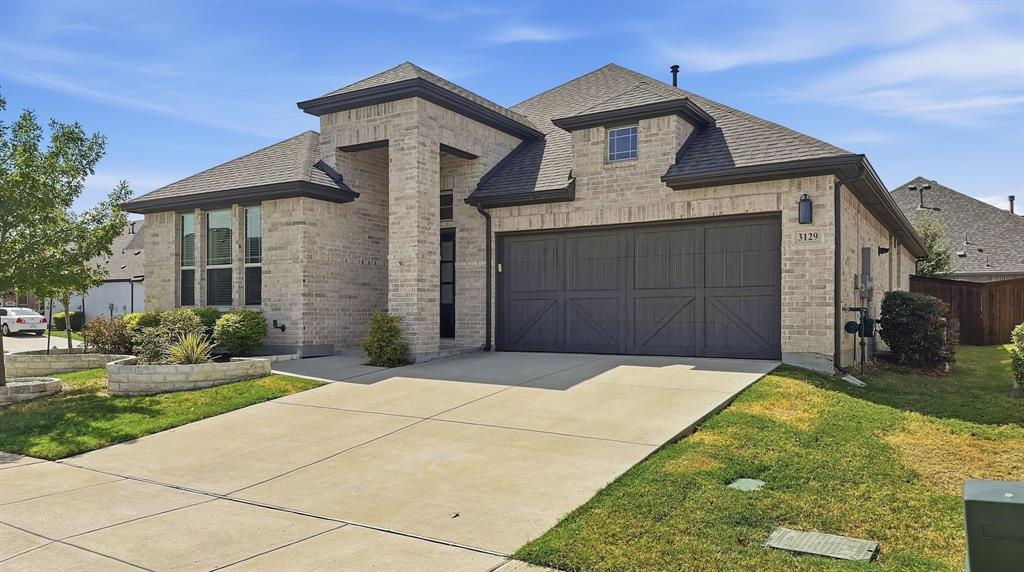 Brick exterior featuring a multi-gabled roofline, oversized two-car garage with decorative cross-buck detailing, and stone-bordered landscaping Brick exterior featuring a multi-gabled roofline, oversized two-car garage with decorative cross-buck detailing, and stone-bordered landscaping
