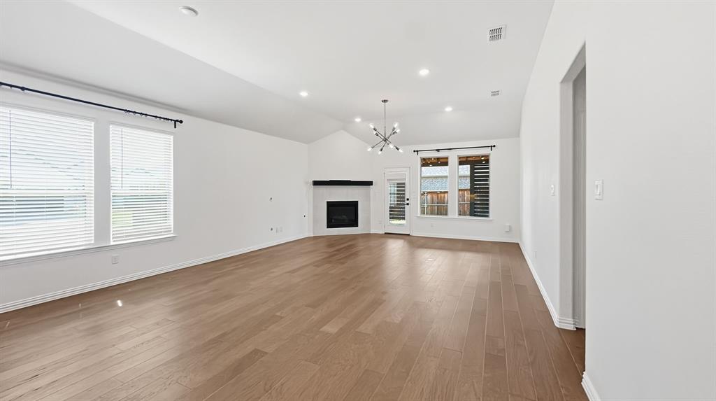 Vaulted ceilings, wood-finish flooring, corner fireplace with a mantel, recessed lighting, and a modern multi-arm chandelier