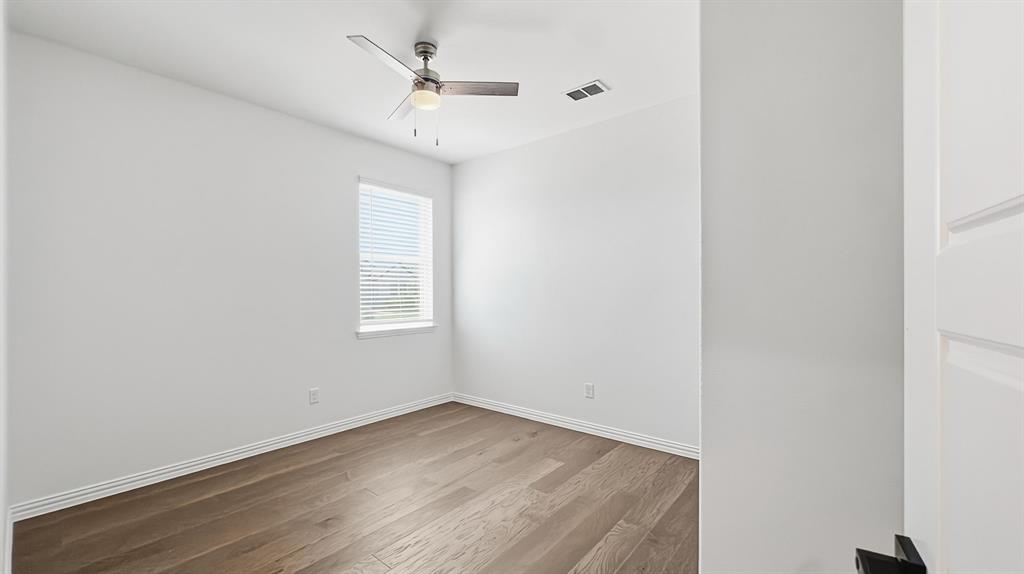 Neutral-toned room featuring wood-finish flooring, a ceiling fan with integrated lighting, and a single-pane window