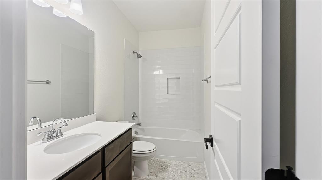 Bathroom featuring a dark-finish vanity with a white countertop, large wall-mounted mirror, tub-shower combination with white subway tile surround and integrated wall niche, and mosaic tile flooring