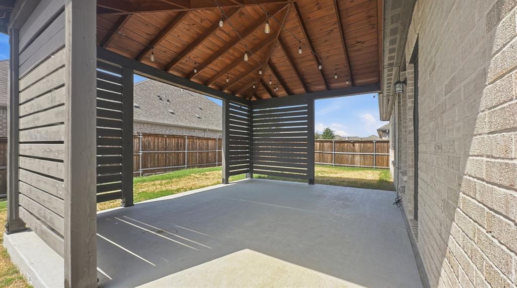 Covered patio featuring a wood-plank ceiling, horizontal slat privacy screens, concrete flooring, and an exterior brick finish