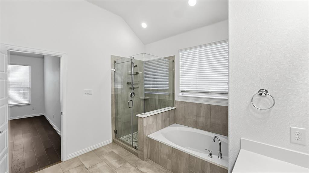 Bathroom featuring a vaulted ceiling, recessed lighting, a tiled shower with a glass enclosure, a built-in soaking tub, and tile flooring