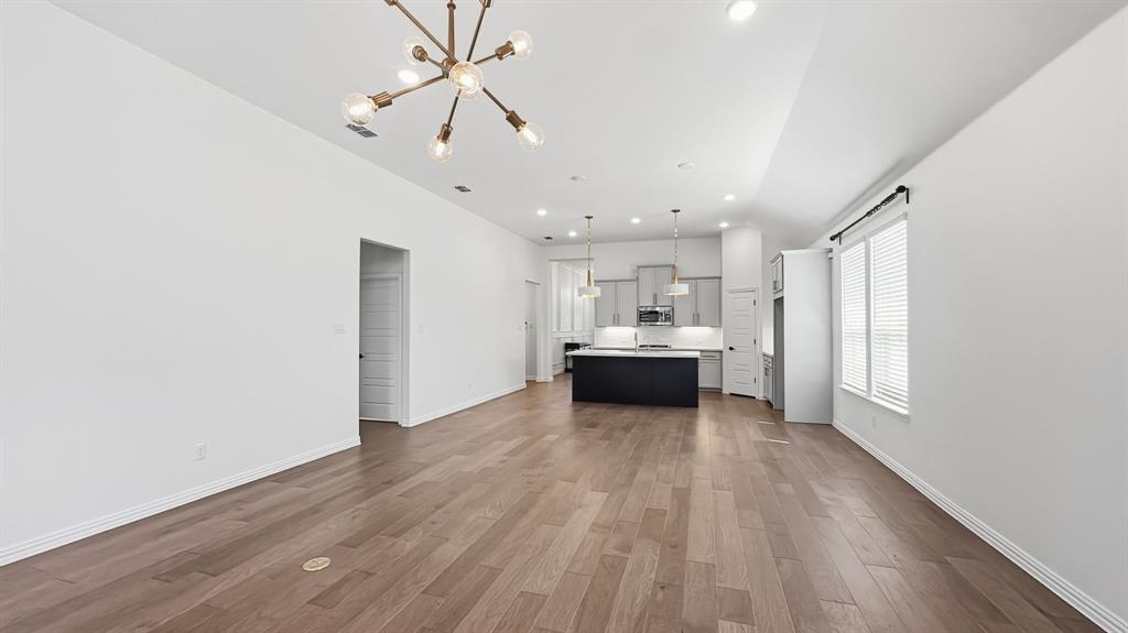 Open-concept interior featuring wood-finish flooring, vaulted ceilings, multi-arm chandelier lighting, and a kitchen island with stone countertops