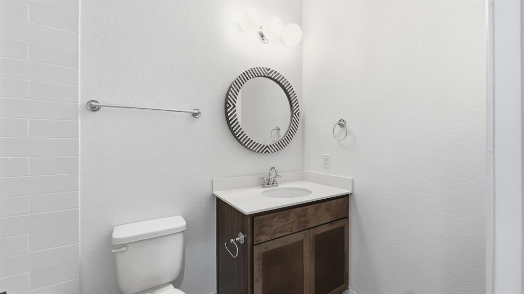Vanity featuring wood-finish cabinetry, a white countertop with an integrated basin, a three-light globe vanity fixture, and a circular decorative wall mirror