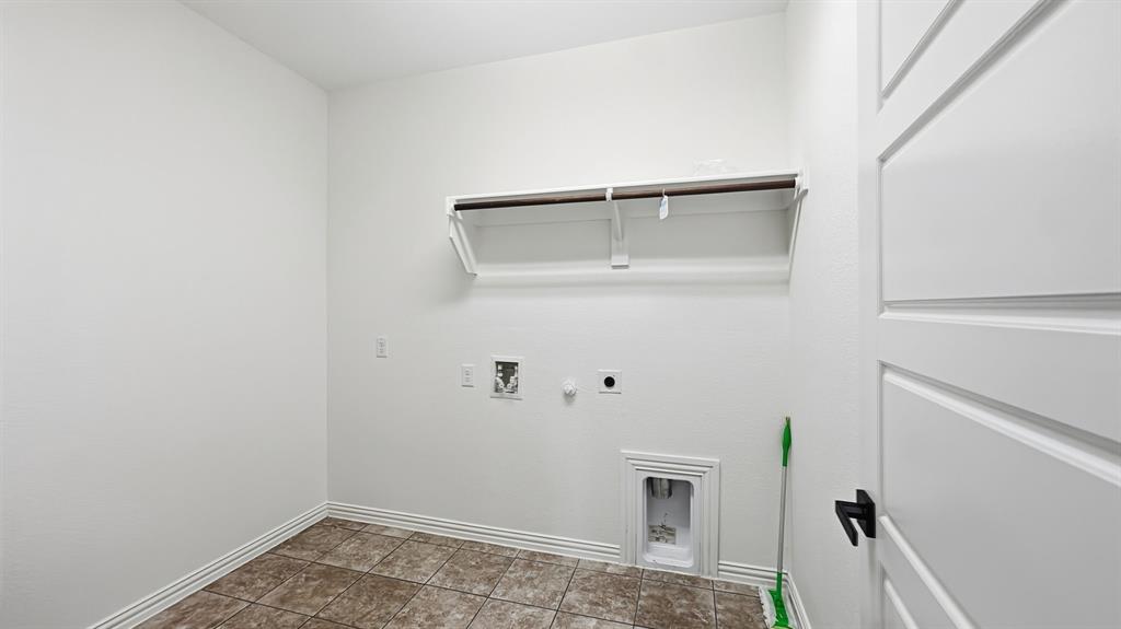 Utility room featuring tile flooring, built-in wall shelving with a hanging rod, and dedicated washer and dryer hookups