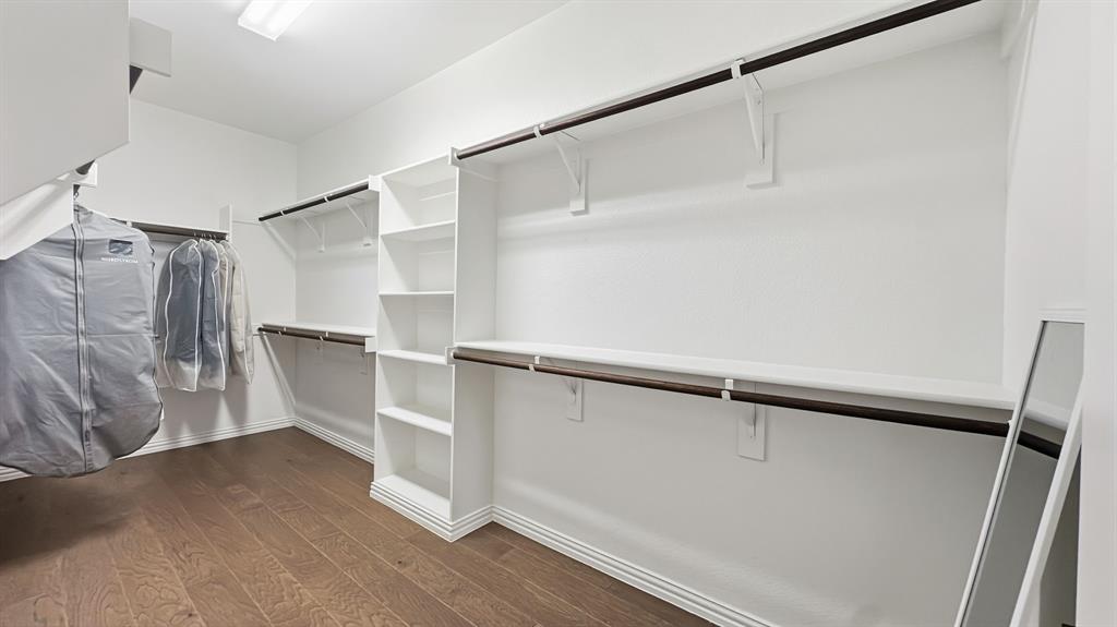 Walk-in closet featuring white built-in shelving, multi-level hanging rods, and wood-finish flooring