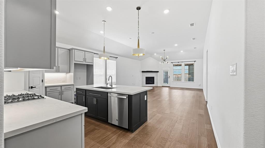 Kitchen featuring a large center island with a quartz countertop, contrasting dual-tone cabinetry, stainless steel appliances, and wood-finish flooring throughout the open-concept space, highlighted by a corner fireplace