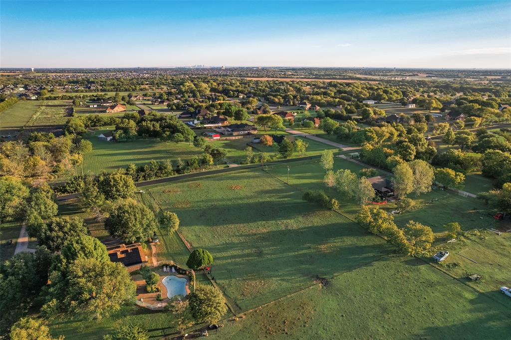 Aerial perspective featuring expansive acreage, mature tree clusters, and a ground-level swimming pool with stone-finish decking Aerial perspective featuring expansive acreage, mature tree clusters, and a ground-level swimming pool with stone-finish decking