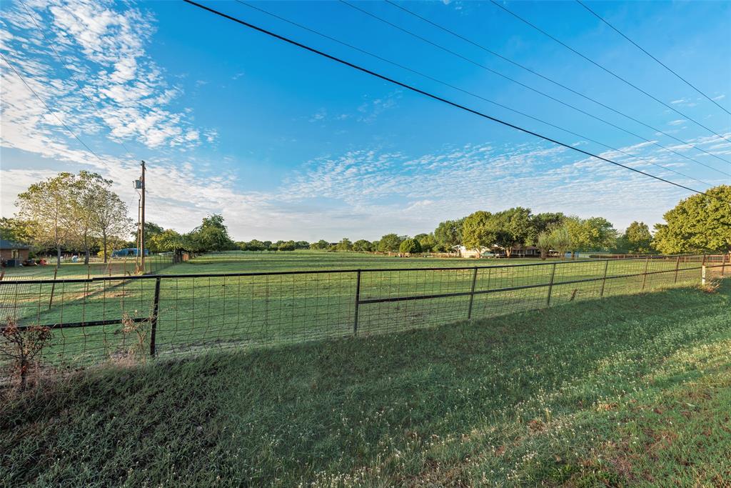 Expansive open acreage featuring manicured grass, mature trees, and wire perimeter fencing