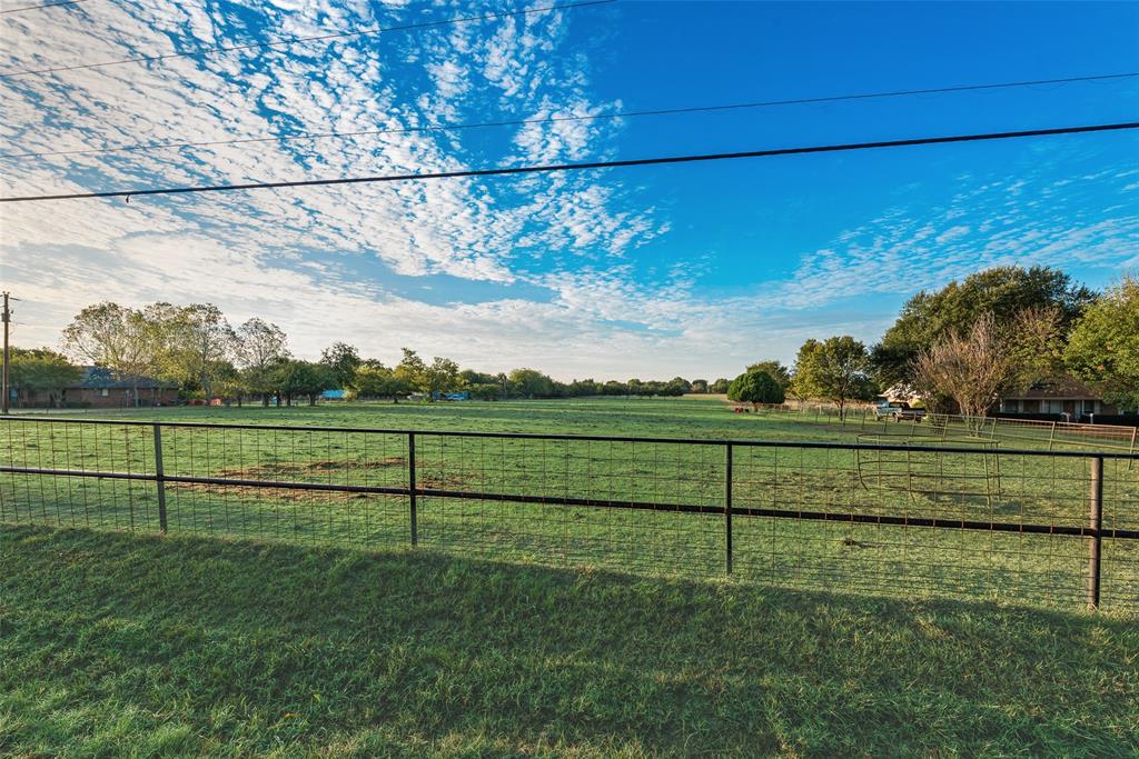 Expansive open acreage featuring manicured grass, mature trees, and wire-mesh perimeter fencing