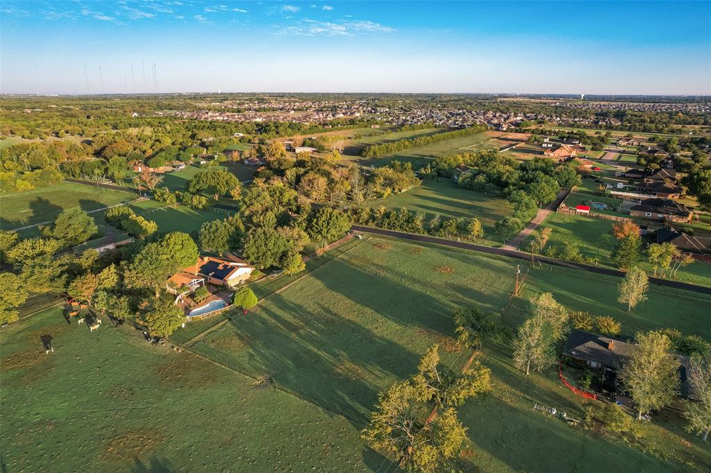 Aerial perspective of expansive acreage featuring mature trees, fenced pasture land, and an in-ground swimming pool Aerial perspective of expansive acreage featuring mature trees, fenced pasture land, and an in-ground swimming pool