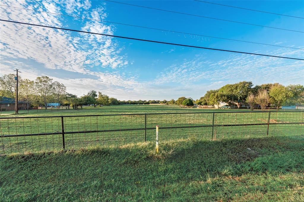 Expansive open pasture featuring a metal grid fence and mature tree clusters