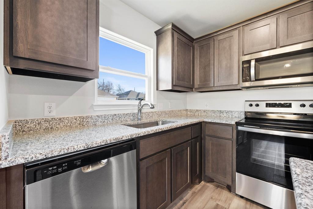 Kitchen with dark brown cabinetry, light stone countertops, sink, light hardwood / wood-style floors, and appliances with stainless steel finishes
