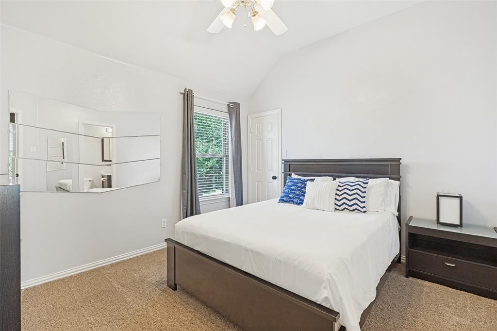 Vaulted ceiling, wall-mounted segmented mirror, window with neutral drapery, six-panel interior door, and ceiling fan with integrated lighting