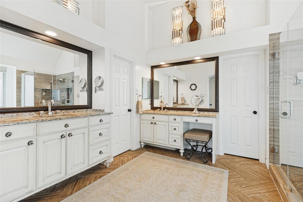 Dual white cabinetry vanities featuring stone-finish countertops, framed mirrors, and herringbone-patterned flooring, complemented by a glass-enclosed shower